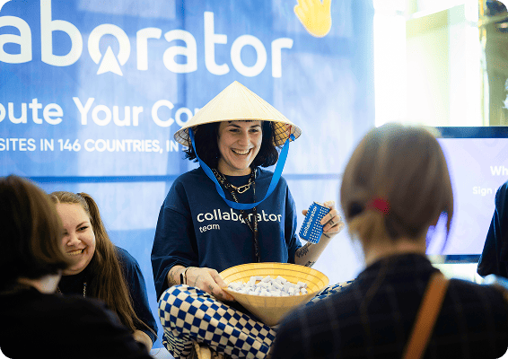 Collaborator team member wearing a traditional Vietnamese conical hat, engaging with attendees at a booth with Collaborator branding in the background promoting global content distribution